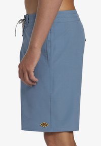 Blauwe zwembroek gemaakt van lichtgewicht stof. Voorzien van een elastische tailleband, trekkoord, zijzakken en een gouden logosticker nabij de zoom.