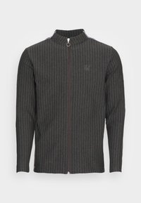 Mörkgrå jacka med vertikala ränder, hög krage, dragkedja framtill och broderad logotyp på vänster bröst. Texturerat tyg.