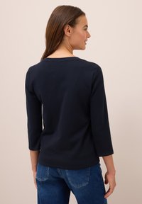 Marineblaues Langarmshirt mit rundem Halsausschnitt, aus weichem Stoff, kombiniert mit hellblauen Jeans aus Denim mit Gesäßtaschen.