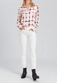 Chemise à boutons crème avec un motif à carreaux rouge et marine, associée à un jean blanc ajusté. Bottines noires à talon bloc.