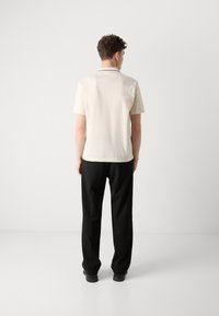 Herren Poloshirt mit kurzen Ärmeln in Cremefarbe und schwarzem Kragenbesatz, kombiniert mit schwarzen Hosen. Glatte Textur und lässige Passform.