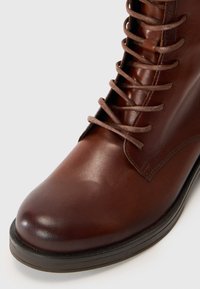 Bottine en cuir marron avec un bout arrondi, dotée de cinq paires d'œillets et de lacets marron, semelle en caoutchouc et détails de couture minimaux.