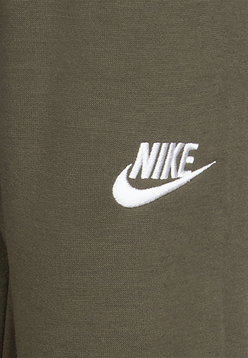 Tissu vert olive avec un logo Nike brodé en blanc et un swoosh. Matériau texturé, gros plan sur le détail du logo.