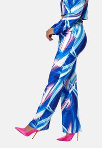 Blue and white patterned crop top with long sleeves paired with wide-leg trousers featuring vibrant blue, pink, and white brushstroke design. Pink stilettos.