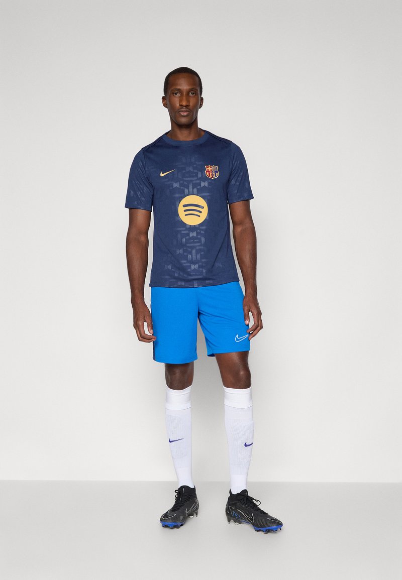 Jersey navy con un patrón gráfico, logo amarillo de Spotify y escudo del Barcelona; combinado con pantalones cortos azul brillante y calcetines blancos. Botas negras.