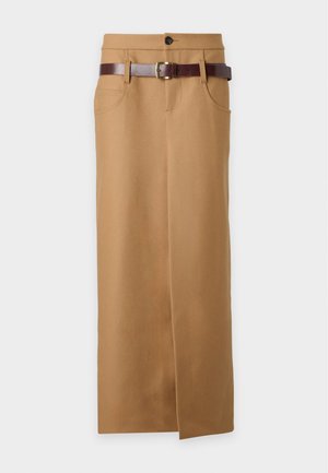 Femme portant un polo gris ajusté à manches courtes et une longue jupe beige fendillée à l'avant, associée à des sandales noires à talons hauts.