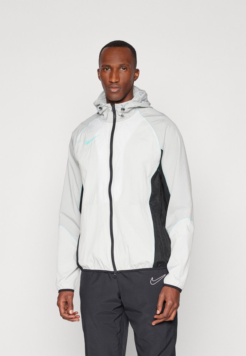 Veste légère à capuche avec un devant blanc, des côtés noirs et des accents menthe. Dispose d'une fermeture éclair sur le devant et de poignets élastiques pour un ajustement.