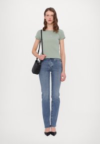 Lichtgroene, korte mouwen t-shirt met een logo, gecombineerd met blauwe rechte spijkerbroeken en zwarte puntige hakken. Zwarte crossbody tas.