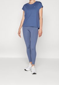 Blue short-sleeve t-shirt with a round neckline, paired with blue leggings. Both made from smooth fabric, complemented by white sneakers.