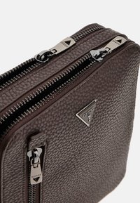 Braune, strukturierte Lederhandtasche mit doppelten Reißverschlüssen und silbernem Metallzubehör; verfügt über ein dreieckiges, metallisches Logo-Detail.