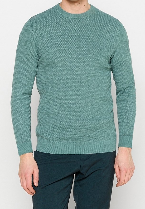 Jersey de punto turquesa con cuello redondo, mangas largas y puños acanalados. Tejido texturizado, estilo ajustado, combinado con pantalones verde oscuro.