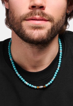 Perlenkette aus türkisfarbigen und braunen Steinen mit silbernen Abstandshaltern, getragen von einem Mann mit kurzem Bart und schwarzem Rundhalsshirt.