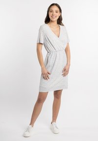 Robe portefeuille à fleurs bleu clair avec des manches courtes, un décolleté en V, une taille élastique et une longueur jusqu'aux genoux. Associée avec des baskets blanches.