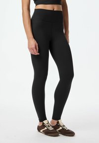 Svarta leggings med hög midja, tillverkade av stretchy tyg. Slät struktur, åtsittande form, kombinerade med bruna sneakers med krämfärgade detaljer.