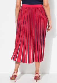 Jupe midi plissée rouge, avec des accents bleu marine et blanc. Présente une large taille et un design fluide atteignant le milieu du mollet, associée à des talons hauts.
