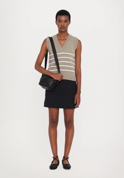 Beežist kudumist ilma varrukateta sviiter valgete triipudega, koos musta mini seelikuga. Mudel hoiab musta õlakotiga ja kannab musti litasid.