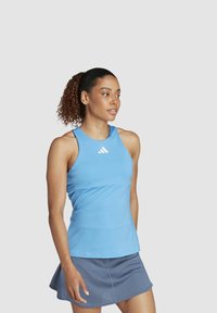 Top atlético azul sin mangas con escote redondo, que presenta un pequeño logotipo blanco. Combinado con una falda gris con un dobladillo acampanado.