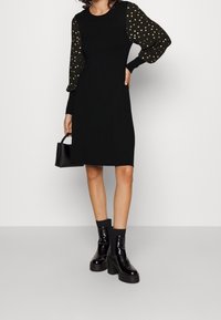 Svart klänning med långa ärmar och guldprickar, en figurnära bodice och rak skärning. Bärs med svarta klackade ankelboots.