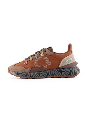 Bruine en beige sneaker met een zwart patroonzool, meerkleurige bedeltjes aan de veters en een grote gestileerde letter "a" aan de zijkant.