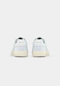 Pair of white low-top sneakers with beige soles shown from the back, featuring "SINCE 1973" printed in gold on each heel tab.