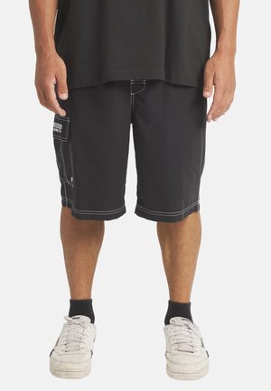 Black shorts made of lightweight fabric with white stitching, featuring a side pocket and relaxed fit. Worn with white sneakers and black socks.