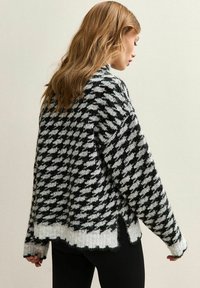 Zwart-wit houndstooth-patroon trui met een geribde zoom, brede mouwen en een ontspannen pasvorm. Zachte gebreide stof met een gestructureerde afwerking.