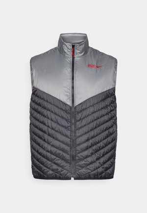 Chaleco sin mangas tipo puffer con cremallera frontal, sección superior en gris claro, sección inferior acolchada en gris oscuro, y logo rojo de "ATLETI" con el swoosh de Nike.