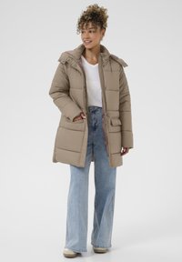 Beige polstret jakke med hætte, der har lynlås og knaplukning, sidelommer og en kontrasterende inderside, parret med lys blå flared jeans.