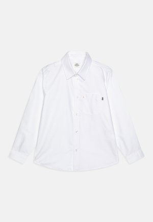 Bela srajca z dolgimi rokavi iz bombaža, z ovratnikom na gumbe, enim žepom na prsih s barvnim akcentom in ravnim robom.