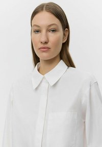 White button-up shirt with a pointed collar, long sleeves, and a chest pocket. Smooth texture, tailored fit, and classic design.