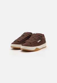 Brune suedesneakers med rund tå, snøredesign, hvit gummimidtsåle og gummisåle. Har en liten merkeetikett.