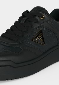 Μαύρο δερμάτινο αθλητικό παπούτσι Guess με ανάγλυφο μοτίβο λογοτύπου, χρυσή τριγωνική ετικέτα της μάρκας και μαύρα κορδόνια σε χοντρή σόλα.