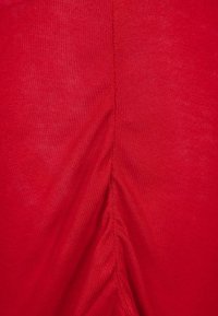 Roter Stoff mit einer glatten Textur, der eine zentrale Naht aufweist, die einen gerafften Effekt erzeugt. Das Material wirkt leicht und dehnbar.