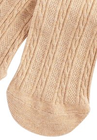 Beige gestrickte Socken mit einem Zopfmuster, gerippten Bündchen und einer glatten Textur, mit abgerundeten Zehen und einer engen Passform.