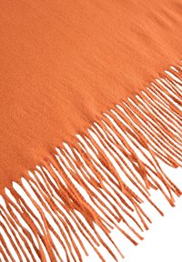 Oranssilla frangeilla varustettu peitto, joka on valmistettu pehmeästä kankaasta. Siinä on siististi leikattu frangi toisella reunalla ja sileä, hieman teksturoitu pinta.