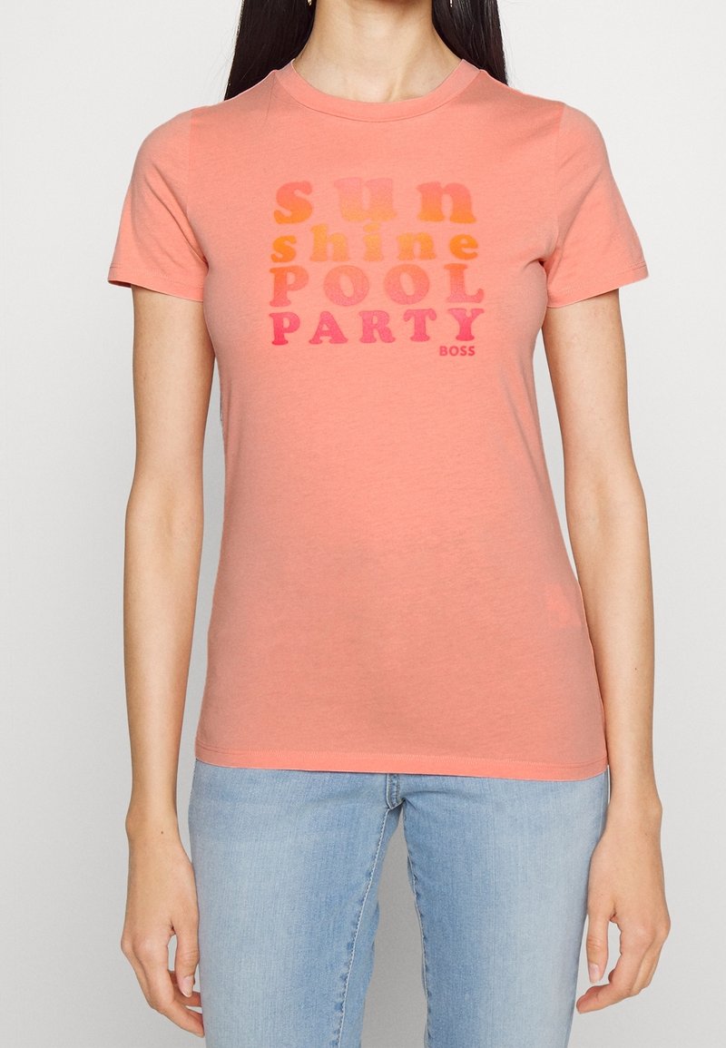 Rosa bomullströja med korta ärmar, prydd med texten "sun shine POOL PARTY" i gradientfärger och en liten logotyp för varumärket.