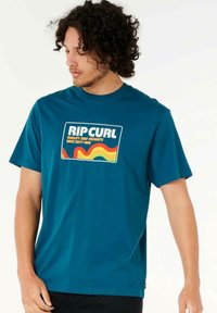 Teal bomulds t-shirt med et grafisk design, der har teksten "RIP CURL" og retro bølgemønstre i gul, rød og orange farver.