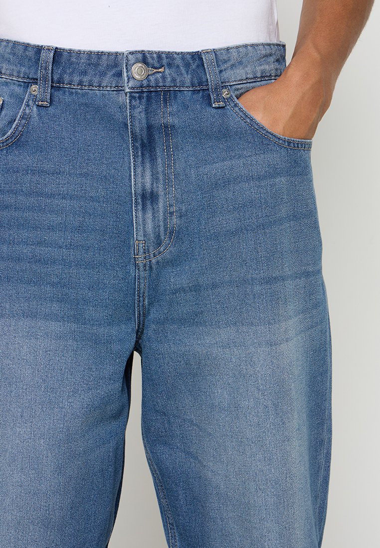 Hellblaue Jeans aus Denim mit geradem Schnitt, ausgestattet mit einem vorderen Knopfverschluss, Gürtelschlaufen und Seitentaschen. Verwaschener Look für Struktur.