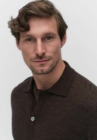 Donkerbruin polo-shirt van textuurstof, met een kraag, een knoopsluiting aan de voorkant met een lichtblauwe knop en een strakke pasvorm.