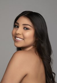 Portrait d'une personne avec de longs cheveux noirs, une peau lisse et un léger sourire. L'arrière-plan est d'une couleur grise neutre.