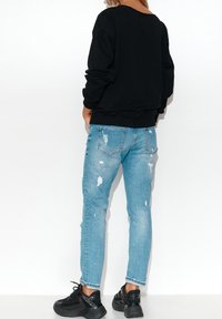 Černá mikina s volným střihem, která se kombinuje s světle modrými džínami s distressed efektem a roztrhanými lemy, a černými teniskami.