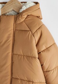 Brun puffjacka med en texturerad, fluffig huva. Slät, quiltad yttertyg med horisontella sömmar och rundad nederkant.