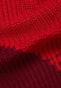 Gestrickter Stoff in Rottönen mit einem strukturierten, gerippten Muster und unterschiedlichen Schattierungen von leuchtendem Rot bis dunklem Kastanienbraun.