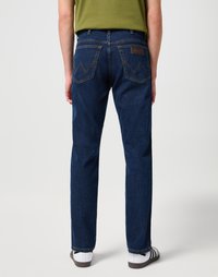 Jeans de mezclilla azul oscuro con corte recto, costuras visibles, dos bolsillos traseros con un patrón de zigzag y un parche de logo de cuero.