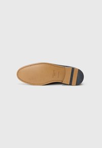 Talpa unei pantofi de piele maro cu toc negru, cusături vizibile și numele brandului "HESCHUNG" imprimat pe toc și talpă.
