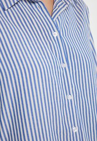 Blauw-wit gestreepte overhemd met knoopsluiting en kraag, voorzien van verticale lijnen en witte knopen langs de voorkant.