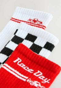 Tri par socka: jedan bijel sa crvenim prugama i logom automobila, jedan crno-bijeli kockasti, i jedan crven sa tekstom "Dan utrke".