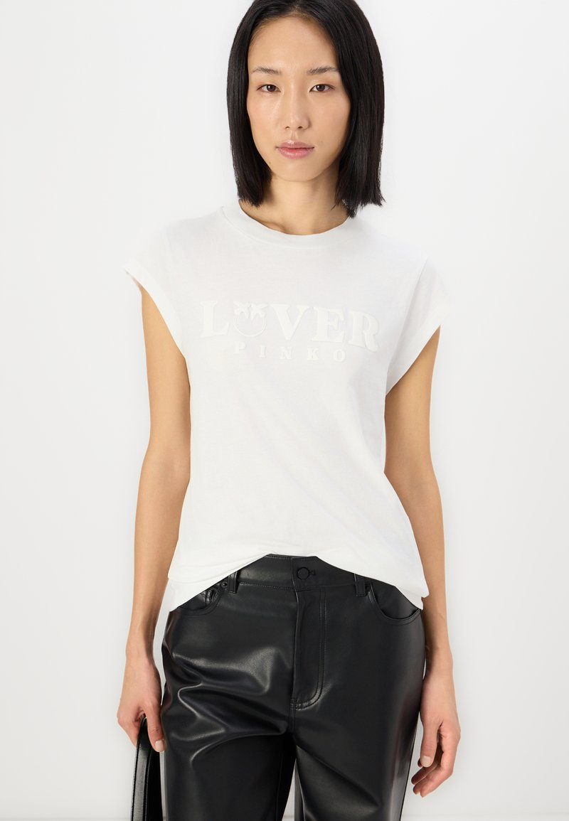 Witte t-shirt met korte mouwen en een verhoogd, lichtgekleurde logo met de tekst "LOVER PINKO" over de borst, gecombineerd met zwarte leren broek.