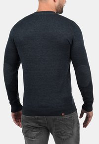 Dark navy sweater with a crew neck, ribbed hem, and elbow patches. Features a smooth texture and fitted design, made from knitted fabric.