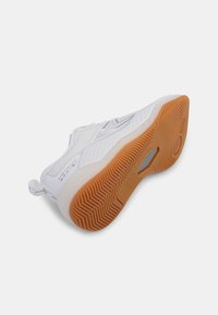 White sneaker with mesh upper, rubber sole, and textured grip. Features a slight heel and a pull tab on the back for easy wear.